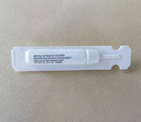 A small, white plastic applicator tube with text printed on it, laying on a beige surface. The text includes a warning to keep out of reach of children and mentions specific usage instructions, often recommended by veterinarians.