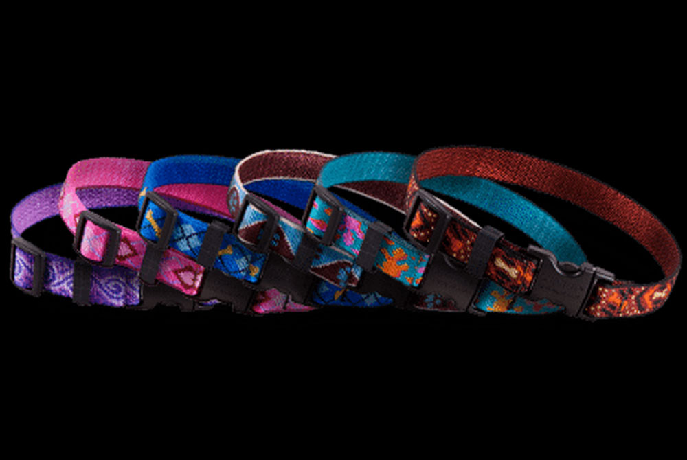 A variety of colorful dog collars arranged in a row against a black background. The collars are made from different patterned materials and feature plastic buckle closures. The colors include shades of purple, blue, teal, and red with various designs, perfect for a stylish look when visiting the vet.